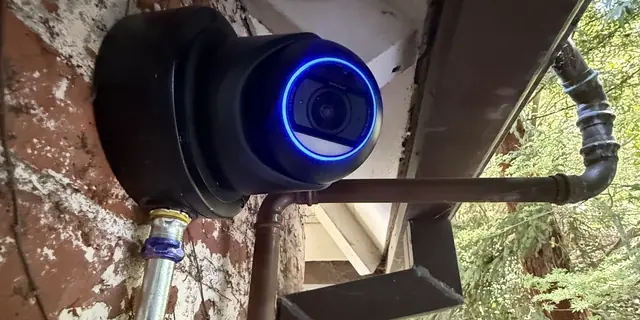 Black UniFi dome camera with a blue ring on a brick wall