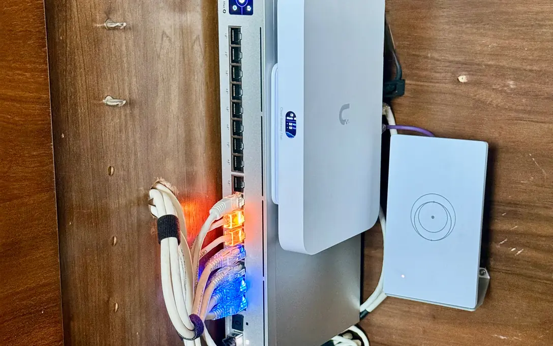 UniFi switch and gateway mounted upright in a wood cabinet