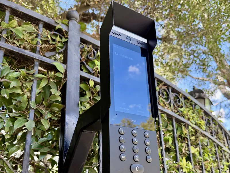 UniFi Access intercom with keypad on a gate pedestal by an iron fence