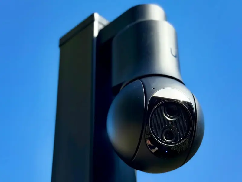 Black dual-lens UniFi camera on a metal post against a blue sky