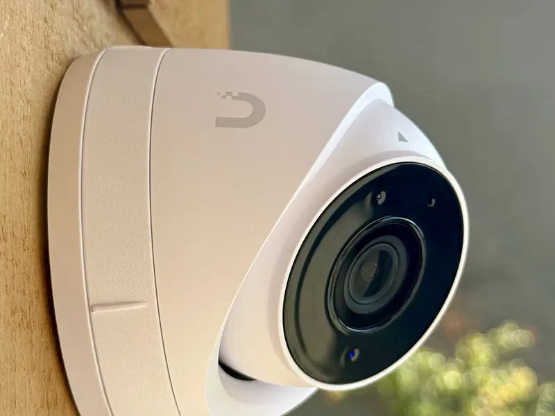 White UniFi turret camera on a wood shingle wall