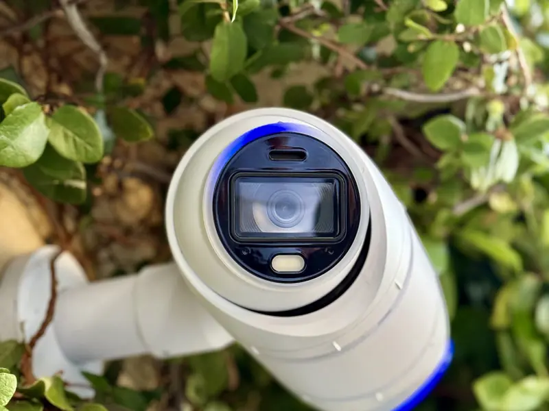 White UniFi bullet camera on a conduit mount in green foliage