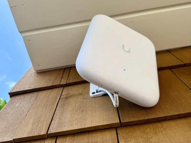 White UniFi outdoor access point on a cedar shingle wall