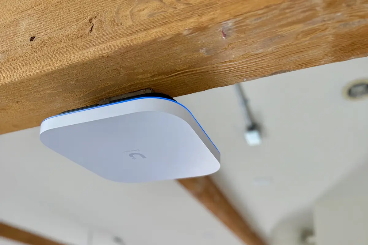 UniFi access point mounted under a wood ceiling beam