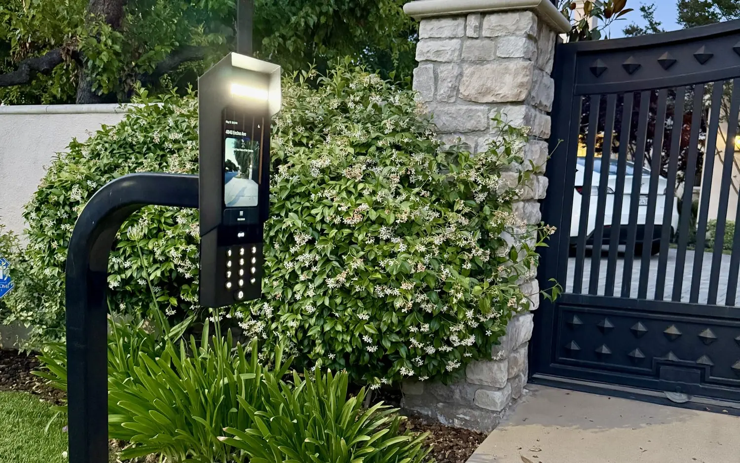 UniFi Access intercom on a pedestal beside a stone pillar and a gated driveway