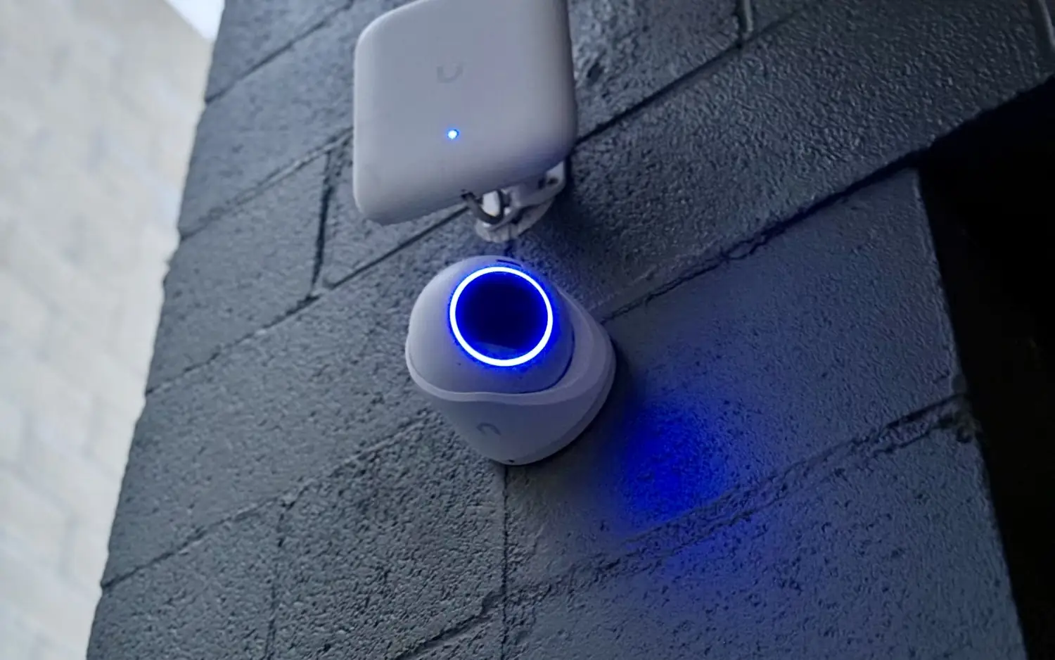 UniFi Protect camera below a floodlight on a block wall