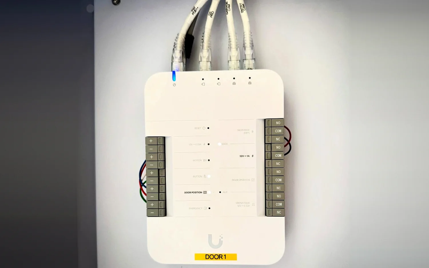 UniFi Door Hub for Door 1 with the lock strike wired to the 12V lock relay, an exit button and door position sensor on the inputs, and power, reader and camera cables in the network ports